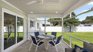 Une terrasse couverte avec une table et des chaises, de grandes fenêtres et une vue sur la cour.
