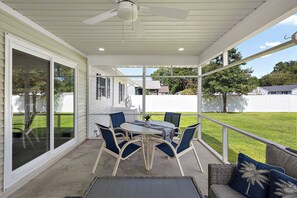 Une terrasse couverte avec une table et des chaises, de grandes fenêtres et une vue sur la cour.