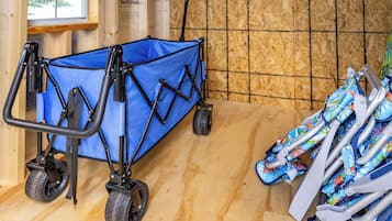 Un carrito utilitario azul con ruedas y un asa, colocado sobre un piso de madera con una pared de fondo con diseño de cuadrícula.