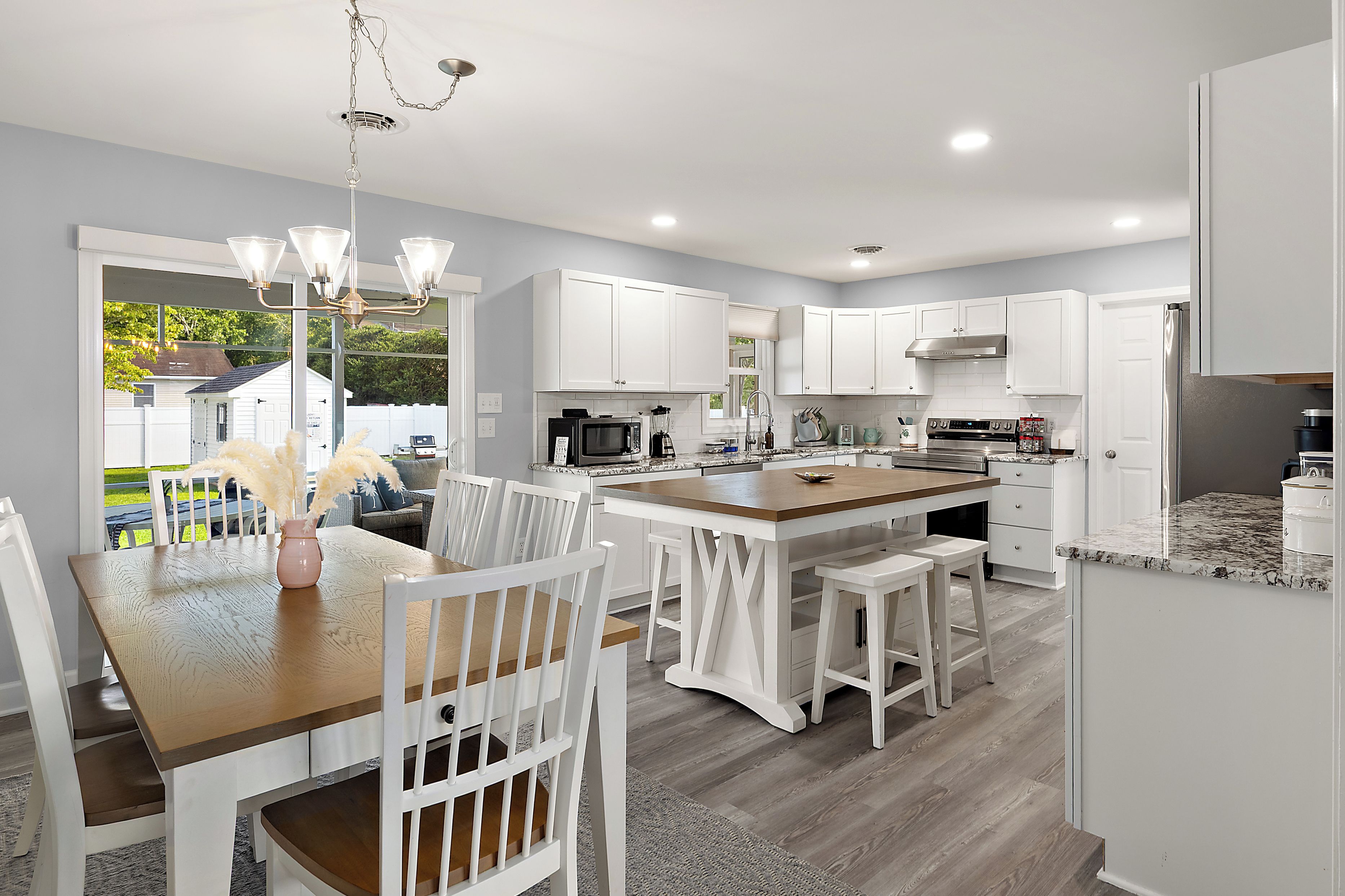 A modern kitchen with white cabinetry, a central island, and a dining area with white chairs and a wooden table.