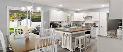A modern kitchen with white cabinetry, a central island, and a dining area with white chairs and a wooden table.