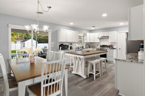 Una cocina moderna con armarios blancos, una isla central y un comedor con sillas blancas y una mesa de madera.