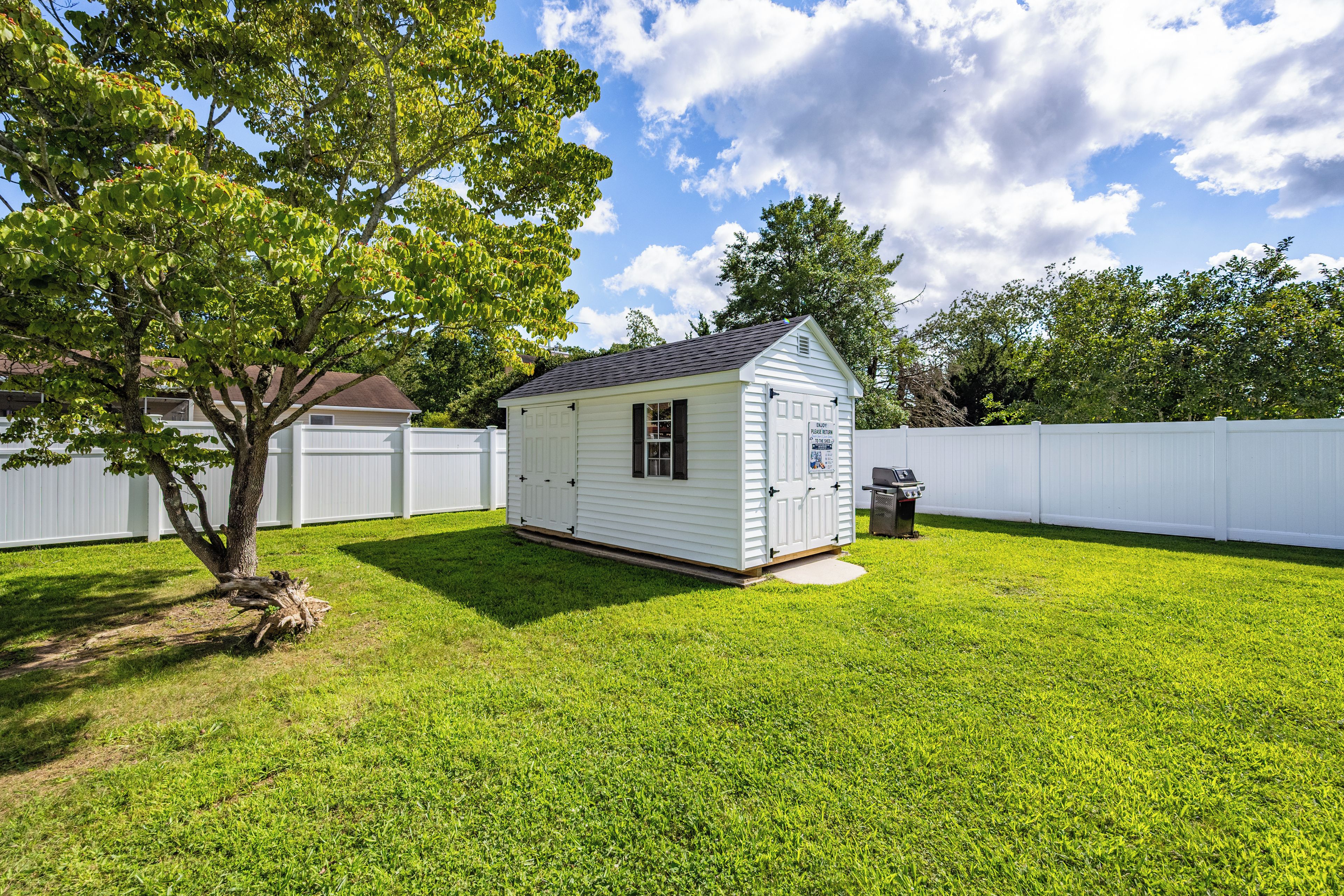 A small, single-story shed with a door and windows, surrounded by a white fence and a well-maintained lawn.
