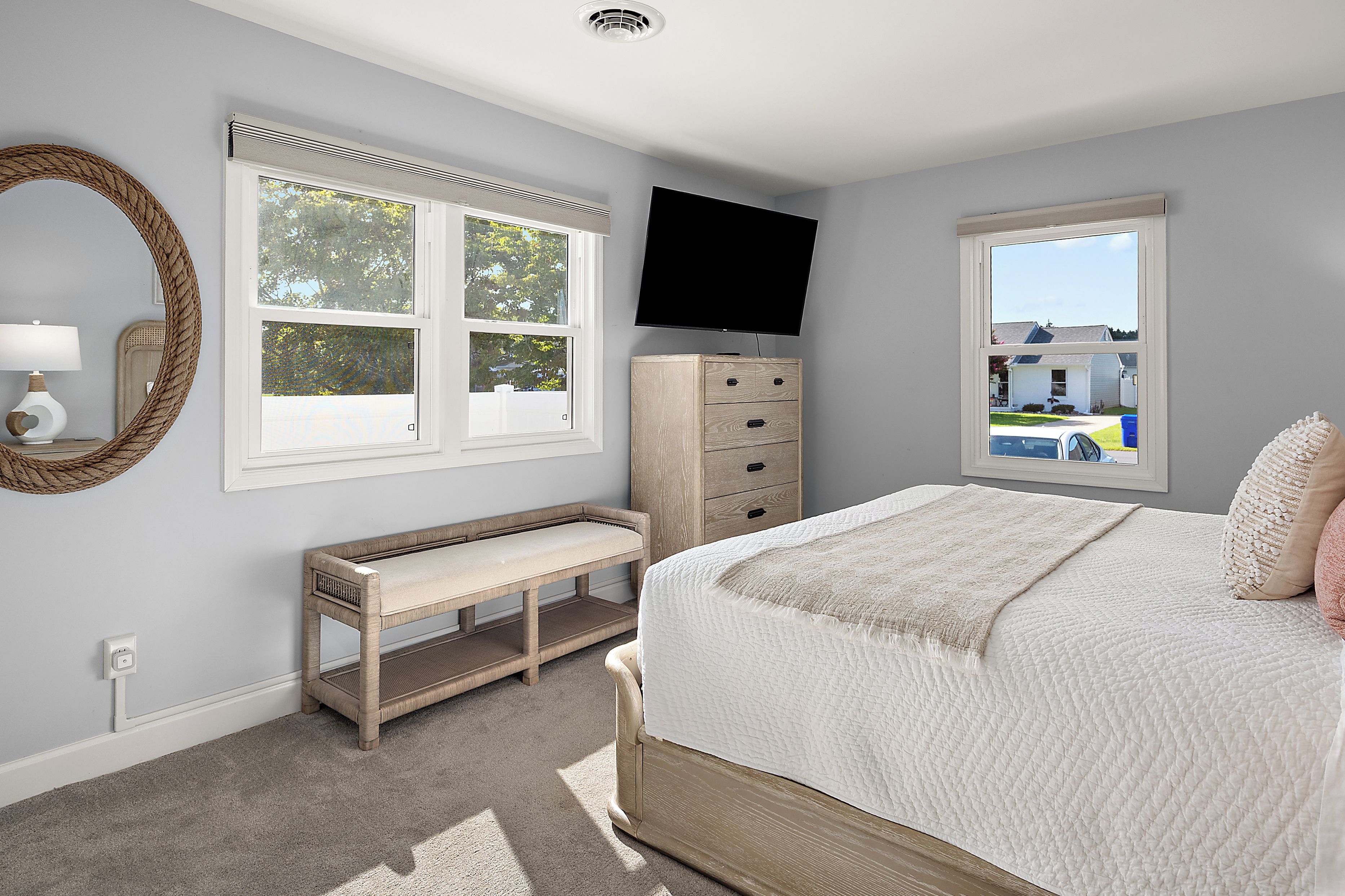 A bedroom with a bed, a bench, a dresser, a television, and two windows.