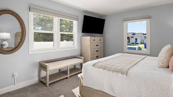 A bedroom with a bed, a bench, a dresser, a television, and two windows.