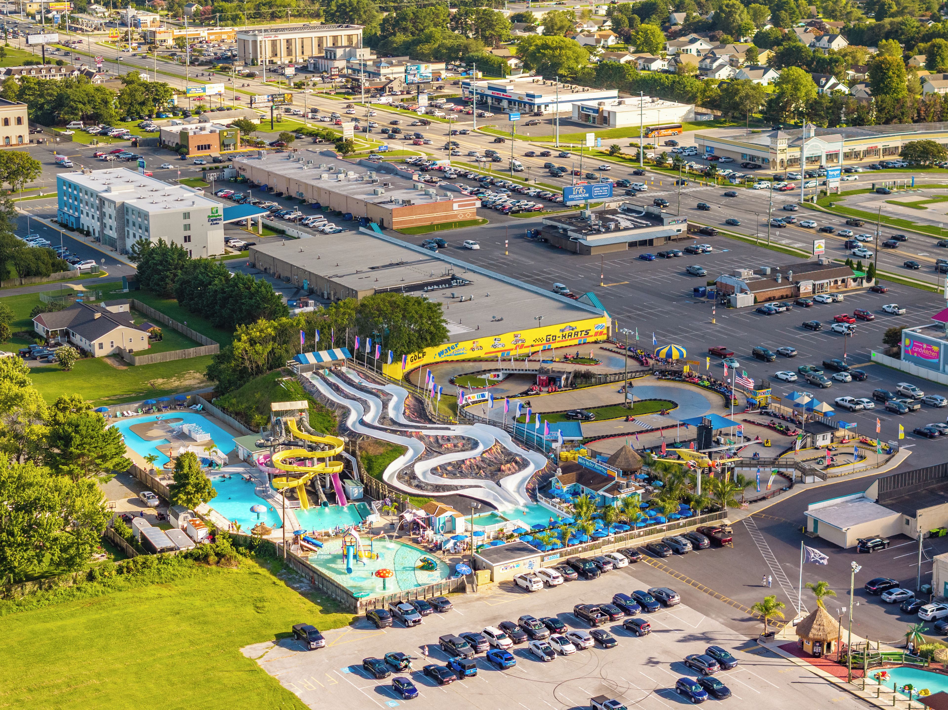 Vue aérienne d’un parc d’attractions comprenant un parc aquatique, des parkings et les bâtiments environnants.