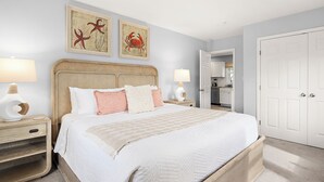 Une chambre à coucher avec un grand lit, deux tables de chevet avec des lampes, une porte et deux tableaux encadrés accrochés au mur.