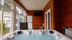 A hot tub with a wooden interior, large windows, and a door leading outside.