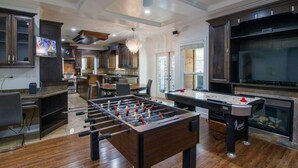 A spacious living area with a foosball table, a pool table, and a television.