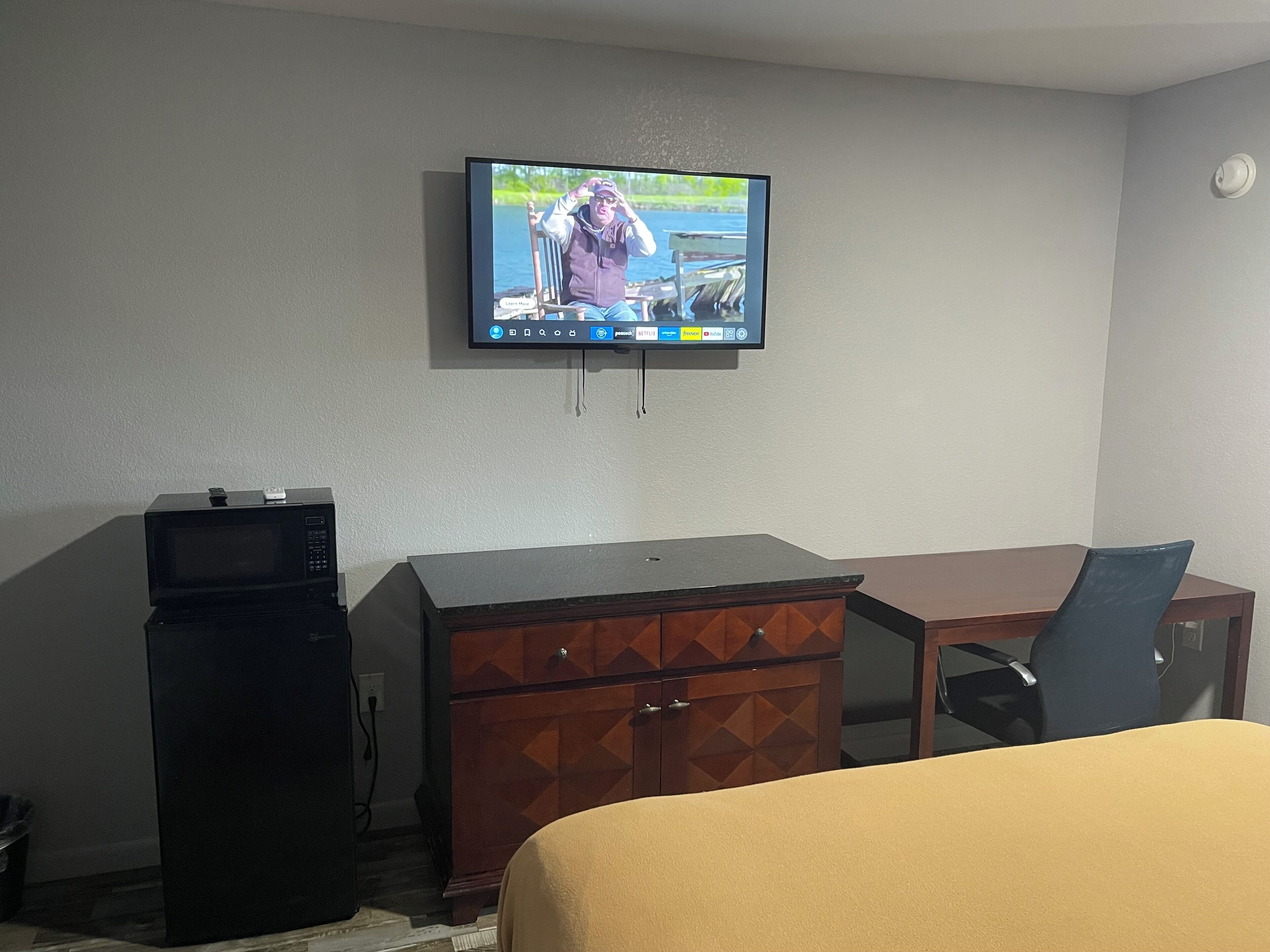 Habitación de hotel con televisor montado en la pared, cómoda de madera, escritorio y cama.