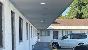 A covered walkway with benches, a parking area with yellow bollards, and a white building with windows. - Newly remodeled 14-room hotel in charming St. Mary's . (St. Marys)