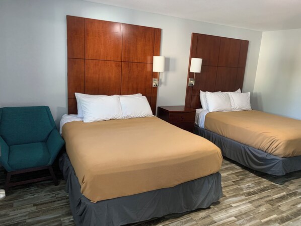 Une chambre d’hôtel avec deux lits, un fauteuil turquoise, des têtes de lit en bois et des lampes de chevet.