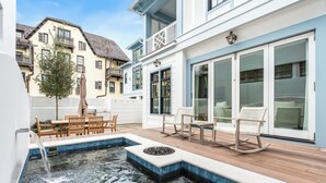 A swimming pool with a waterfall feature, surrounded by wooden deck seating and a small fire pit.