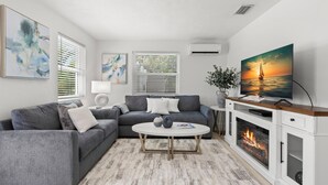 Una sala de estar moderna con un sofá seccional gris, una mesa de centro blanca, una chimenea y un televisor grande sobre un mueble de madera.