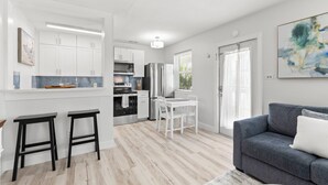 Una cocina moderna con armarios blancos, electrodomésticos de acero inoxidable y una zona de comedor con mesa y sillas blancas.