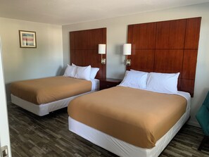 A hotel room with two beds, wooden headboards, bedside lamps, and a framed picture on the wall.