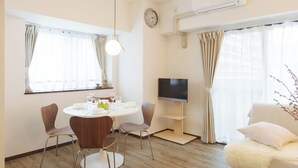 A modern living room with a round dining table, two chairs, a flat-screen TV, a sofa, and a fluffy ottoman. - Baggage OK！Clean, Comfy bed Stay- Dotombori Haven (大阪市中央区島之内2丁目)