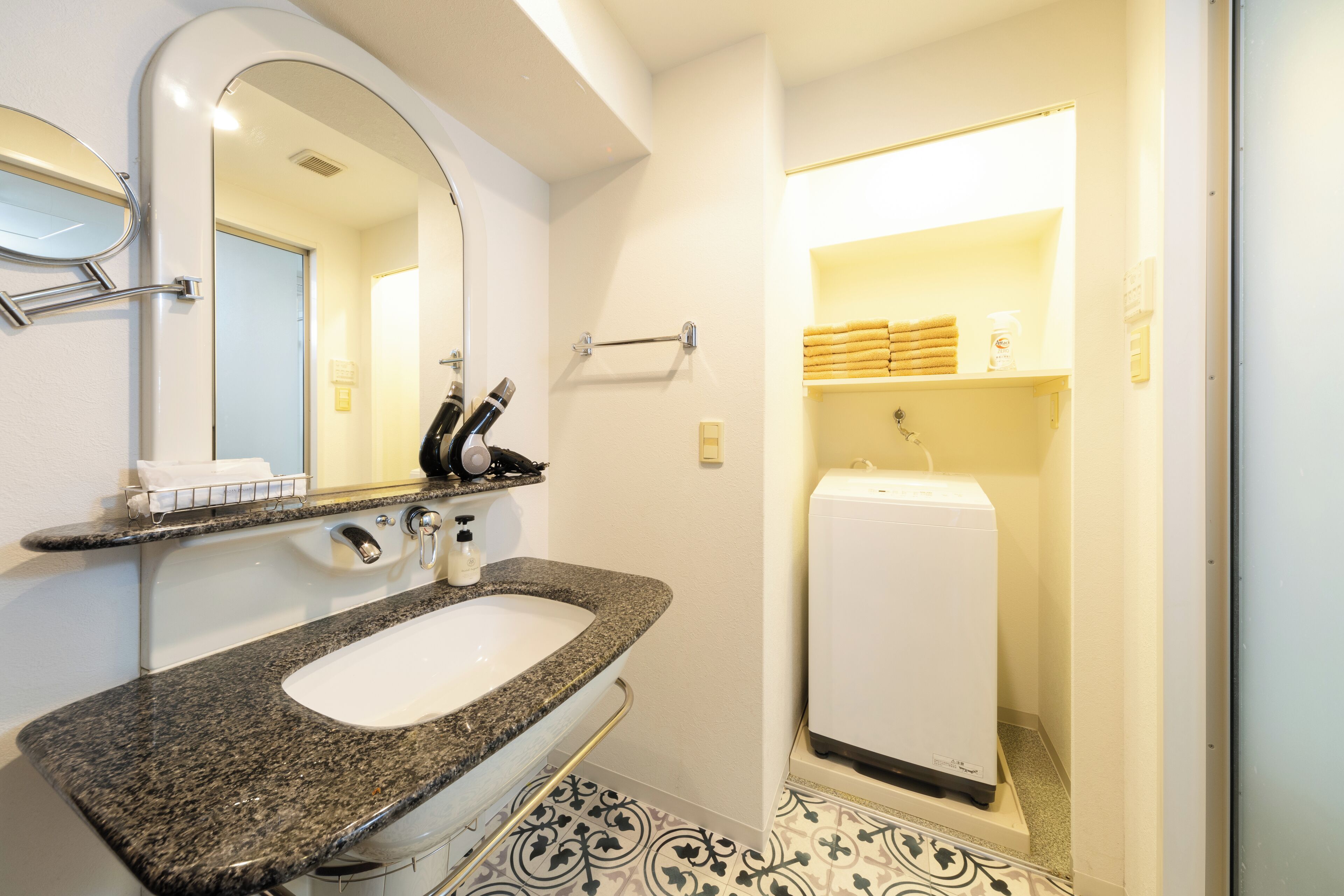 Une salle de bain avec un lavabo doté d’un plan de travail en granit, un miroir, un porte-serviettes et un porte-rouleau de papier toilette.