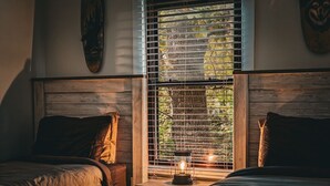 Un dormitorio con dos camas, cabeceros de madera, una mesita de noche con un farol y una ventana con persianas.