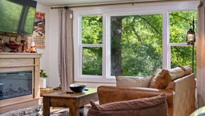 Una sala de estar acogedora con chimenea, un sofá cómodo y grandes ventanales con vistas al exterior.