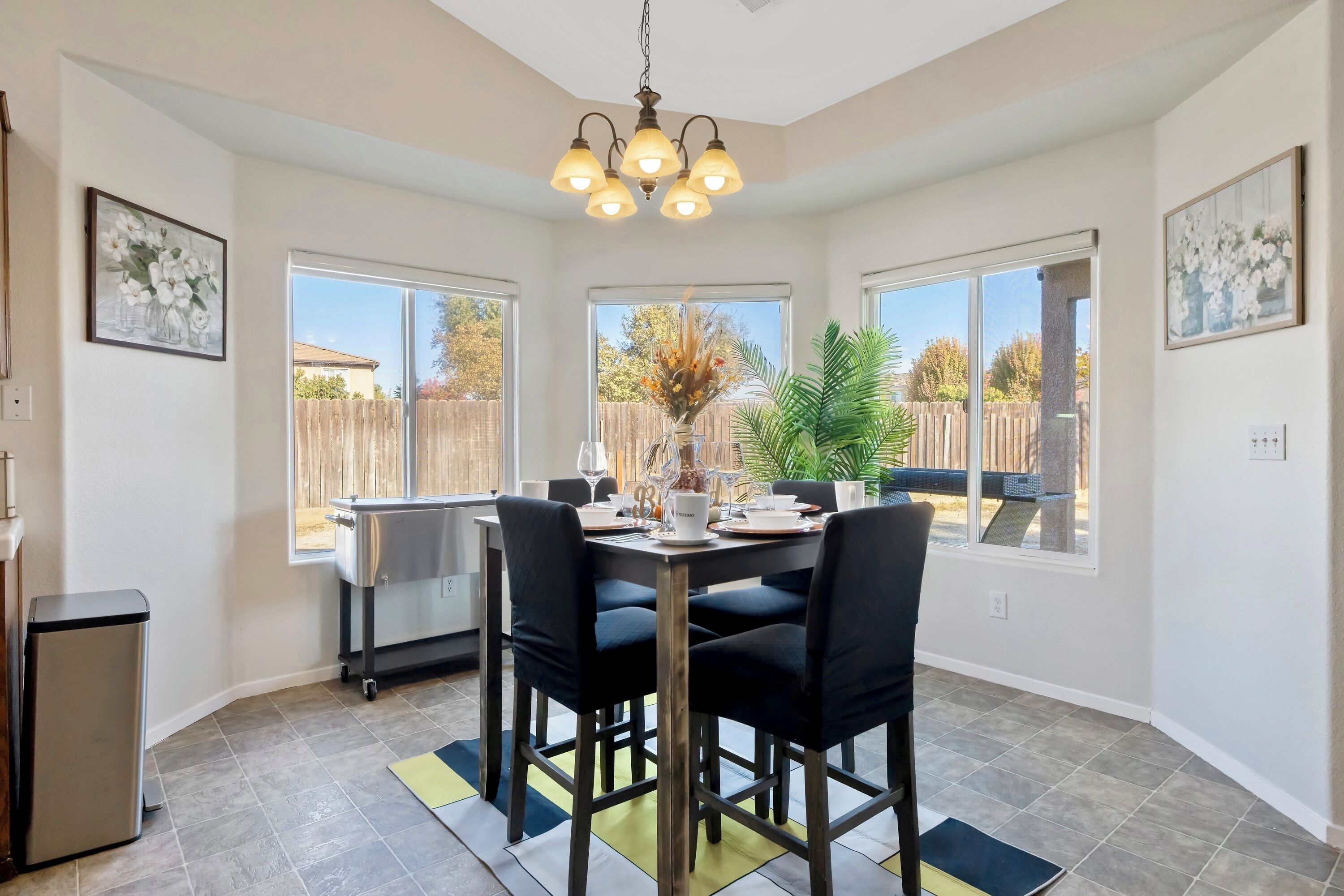 A dining area with a table set for four, a chandelier, and large windows offering a view of the backyard.