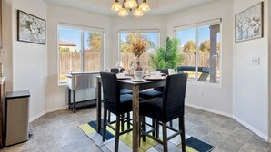 Een eetgedeelte met een tafel voor vier personen, een kroonluchter en grote ramen met uitzicht op de achtertuin.