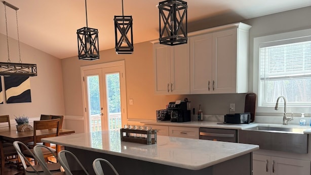Una cocina moderna con una isla grande, armarios blancos e iluminación colgante.