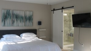 Un dormitorio moderno con una cama grande, un televisor montado en la pared y una puerta corrediza que da a una zona de ducha.