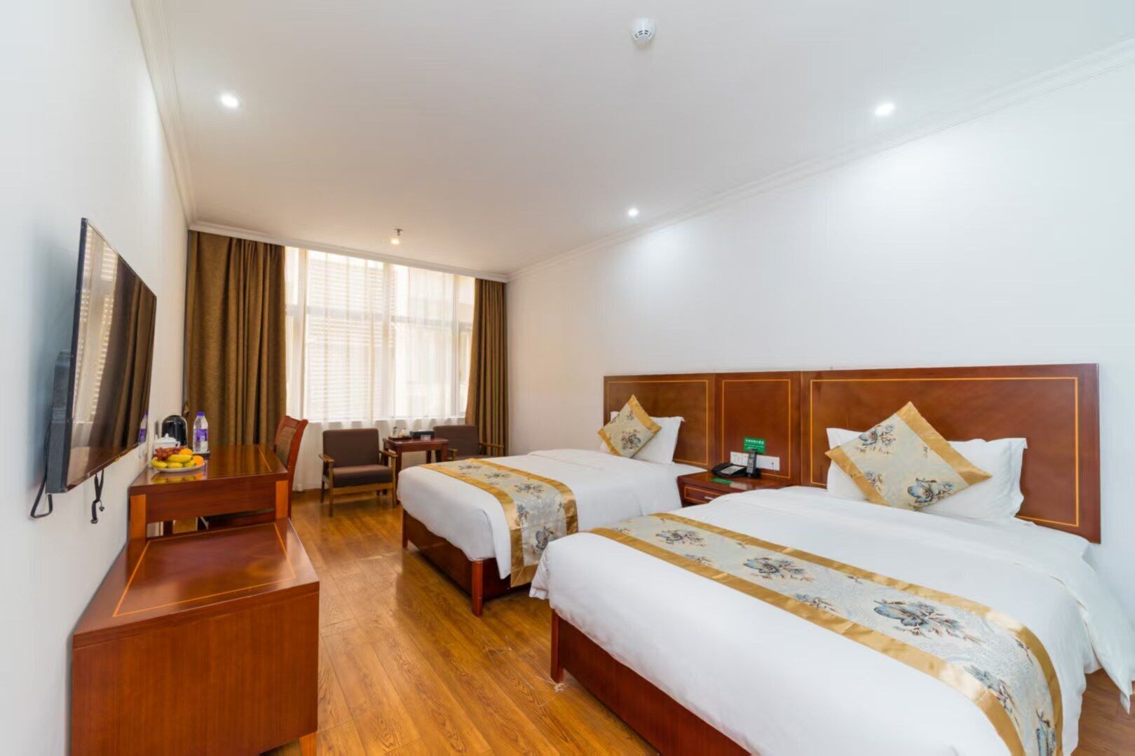 A hotel room with two beds, a desk, a chair, a TV, and a window with curtains.
