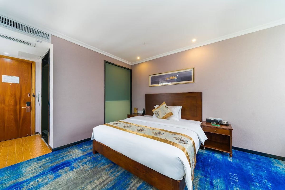 A hotel room with a wooden bed, a nightstand, a wall-mounted phone, and a door with a mirror.