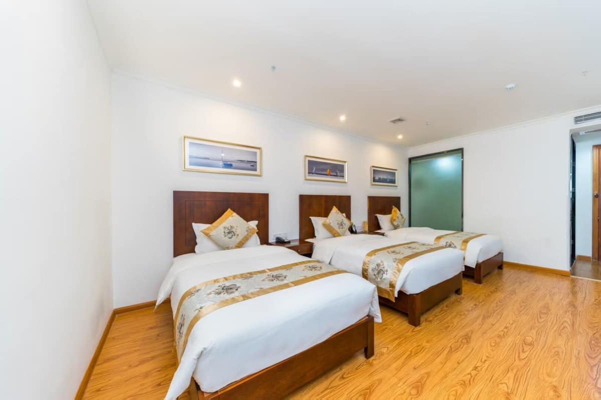 A hotel room with two beds, wooden flooring, and framed pictures on the wall.