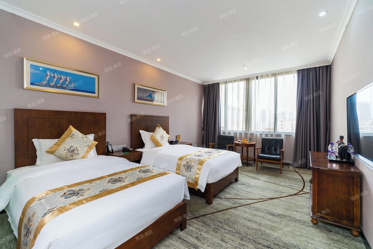 A hotel room with two beds, a desk, a chair, and a TV.