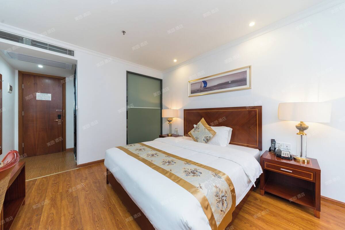 A hotel room with a large bed, bedside tables with lamps, a wooden floor, and a door with a sign.