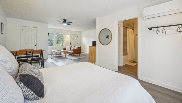 A bedroom with a large bed, a wooden dining table with chairs, a sofa, and a ceiling fan.