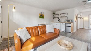 A modern living room with a leather sofa, a coffee table, and a kitchen in the background.