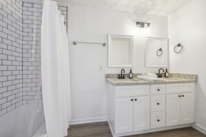 Un bagno con pareti piastrellate di bianco, un lavabo con piano in granito, due specchi e mobili bianchi.