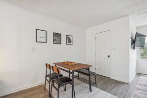 Un'area pranzo con un tavolo e sedie in legno, una porta bianca e quadri appesi al muro.