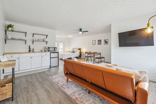 Una cucina moderna con mobili bianchi, un'area pranzo con divano in pelle marrone e una TV a schermo piatto montata a parete.