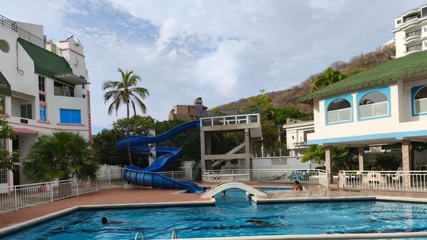 Una piscina con uno scivolo blu, circondata da edifici e palme.