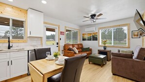 A modern kitchen with white cabinets and a wooden countertop, a dining area with a wooden table and chairs, a brown leather sofa, and a ceiling fan. - Custer Love Shack Getaway (Custer)