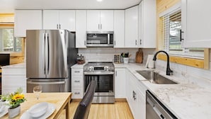 A modern kitchen with white cabinets, stainless steel appliances, a wooden countertop, and a window with blinds. - Custer Love Shack Getaway (Custer)
