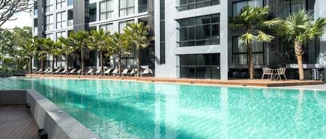 A modern hotel with a swimming pool, lounge chairs, and palm trees.