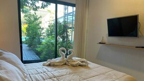 Habitación de hotel con cama, televisor montado en la pared y ventana con vistas a zonas verdes.
