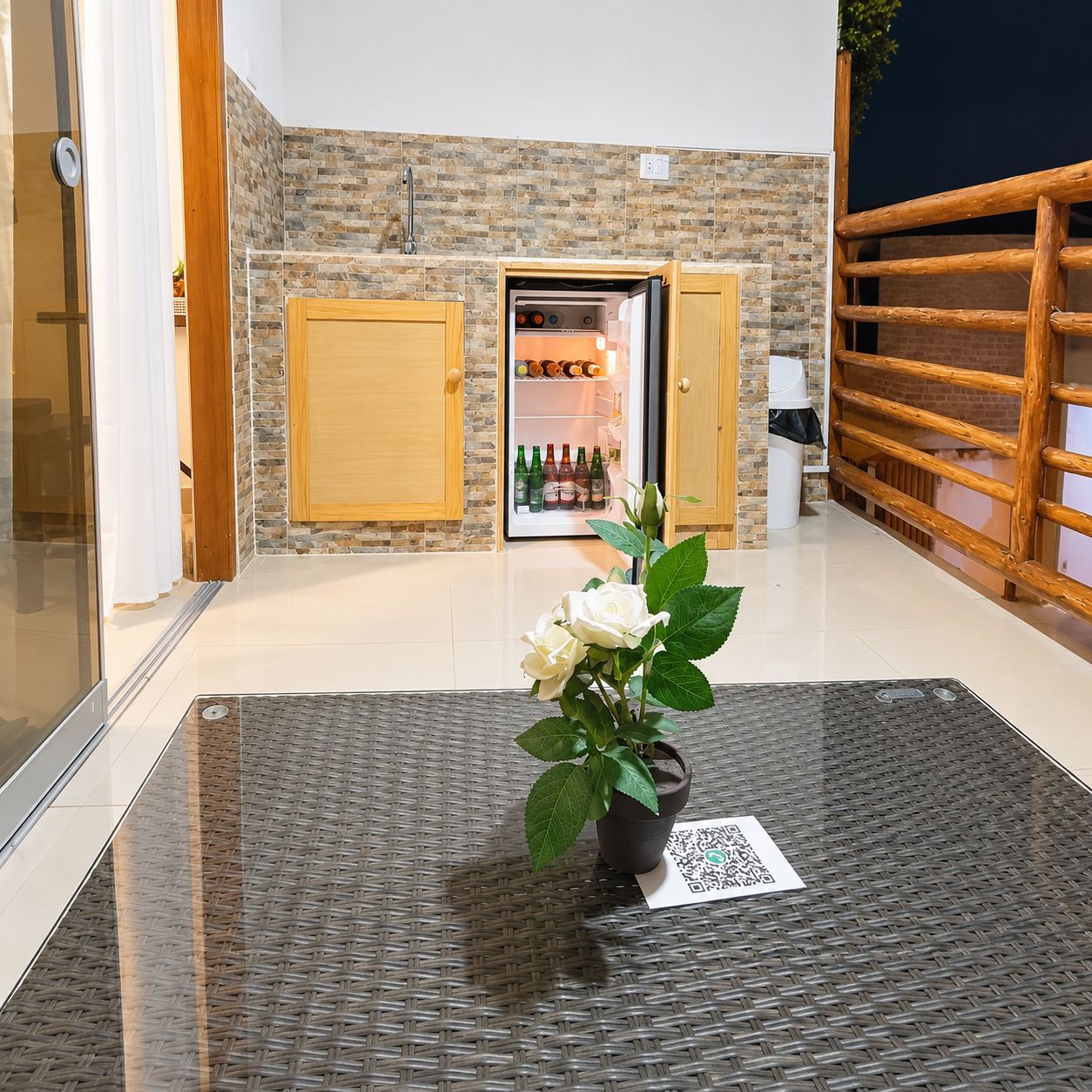 A room with a stone wall, a wooden door, a refrigerator with bottles, and a potted plant on a woven mat.