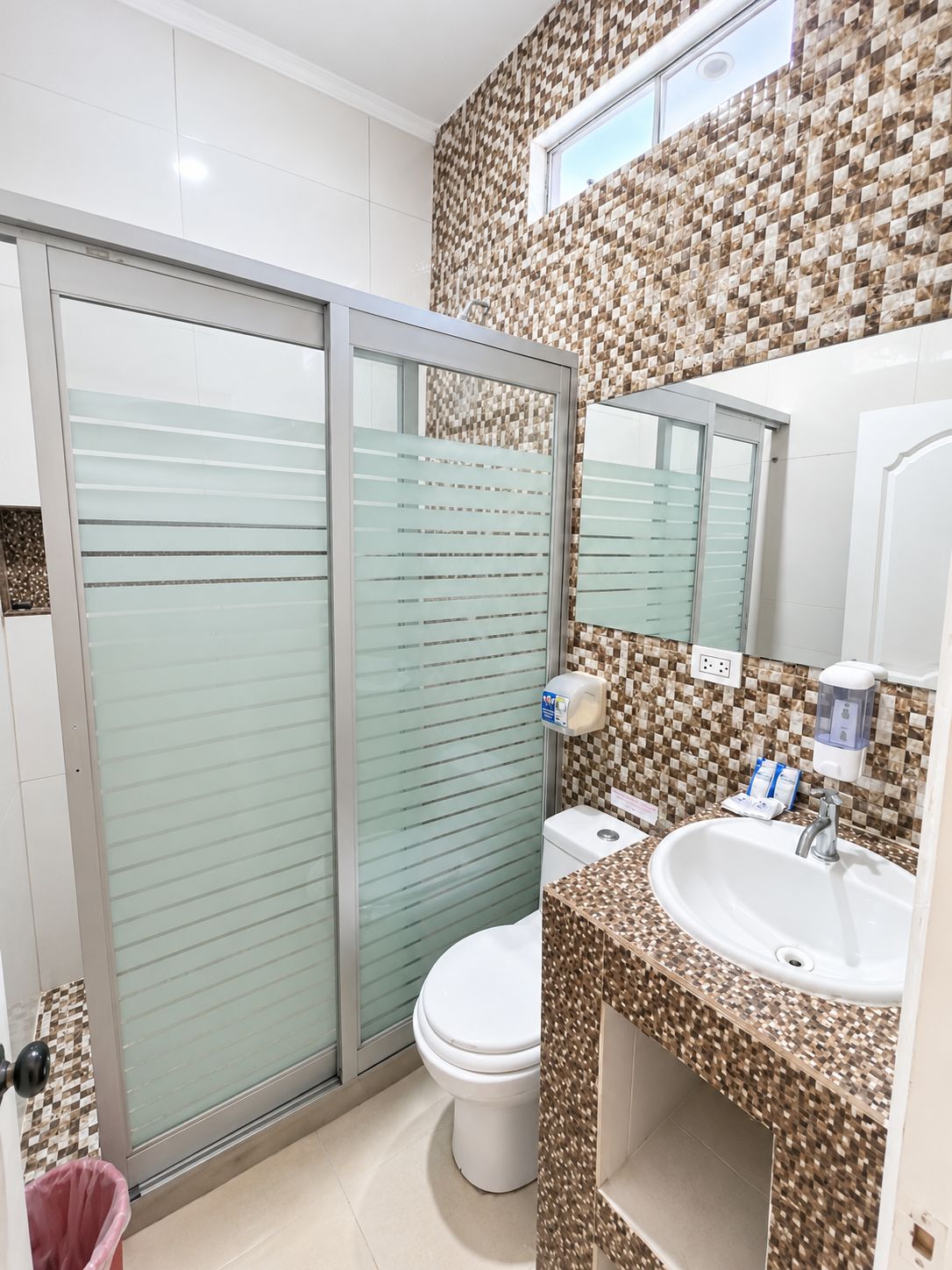 Une salle de bain équipée de toilettes, d’un lavabo et d’une douche avec une porte en verre.
