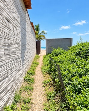A pathway leading to a beach with a wooden fence on one side and a concrete wall on the other.