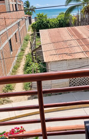 Un balcón con vistas a la costa, incluyendo un edificio en construcción, un techo de lámina corrugada y un camino que lleva a la playa.