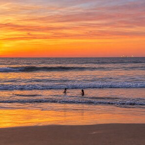 A beach scene at sunset with waves and two people in the water. - Casa 4 habs con aire, piscina y mar a 50 pasos (Zorritos District)