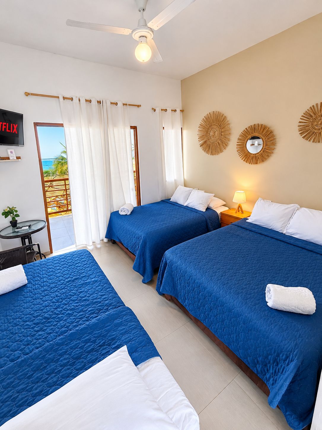 Habitación de hotel con dos camas, televisión, ventilador de techo y vista al mar.