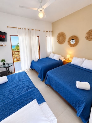 A hotel room with two beds, a TV, a ceiling fan, and a view of the sea.